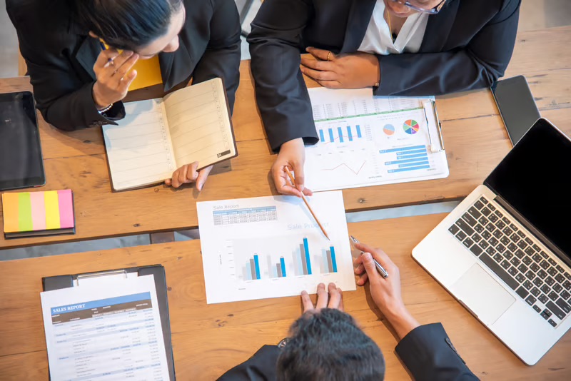 Business professionals reviewing financial reports and sales performance data while evaluating a potential business investment.